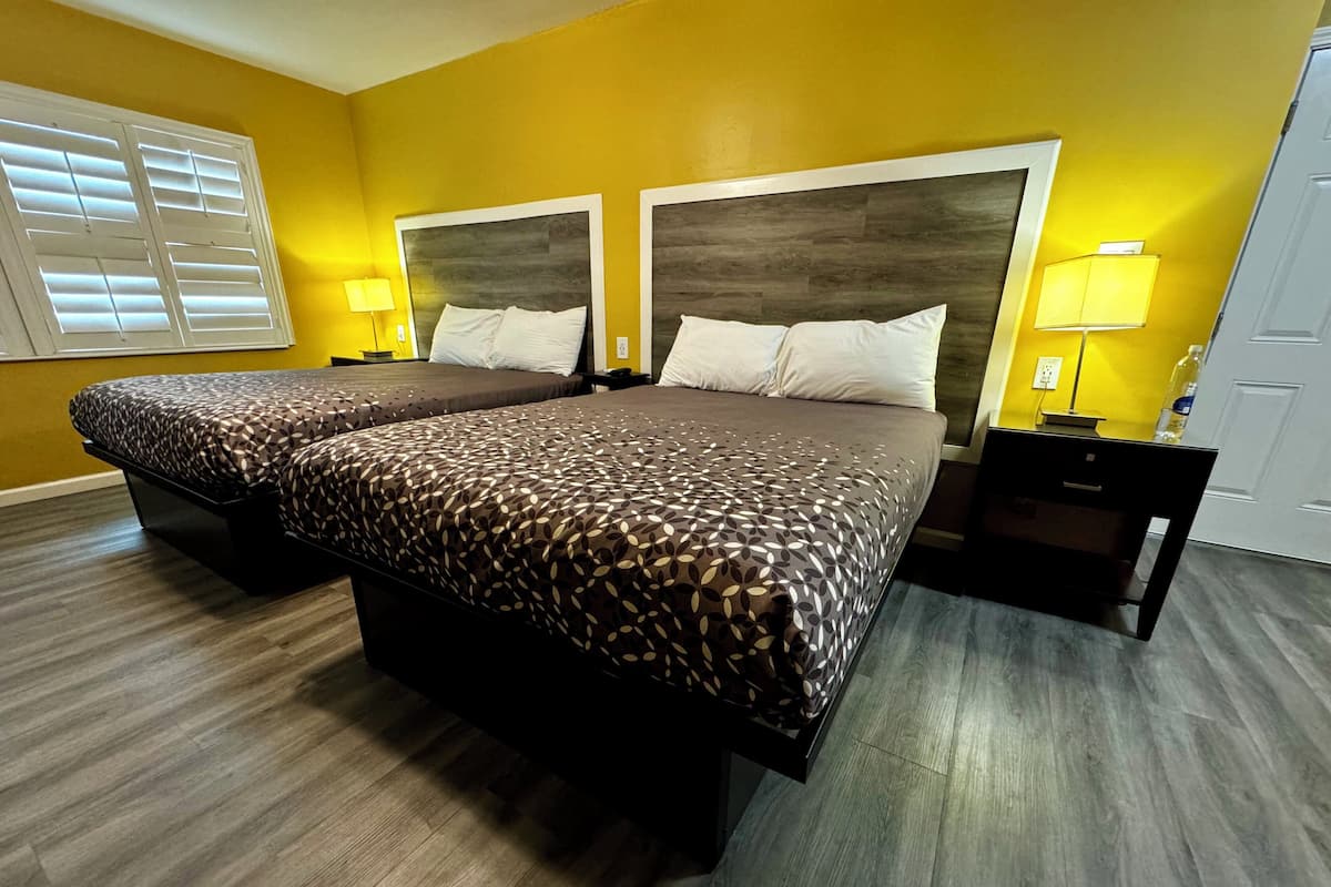 A double bed with a patterned bedspread in a room with yellow walls and wooden flooring.
