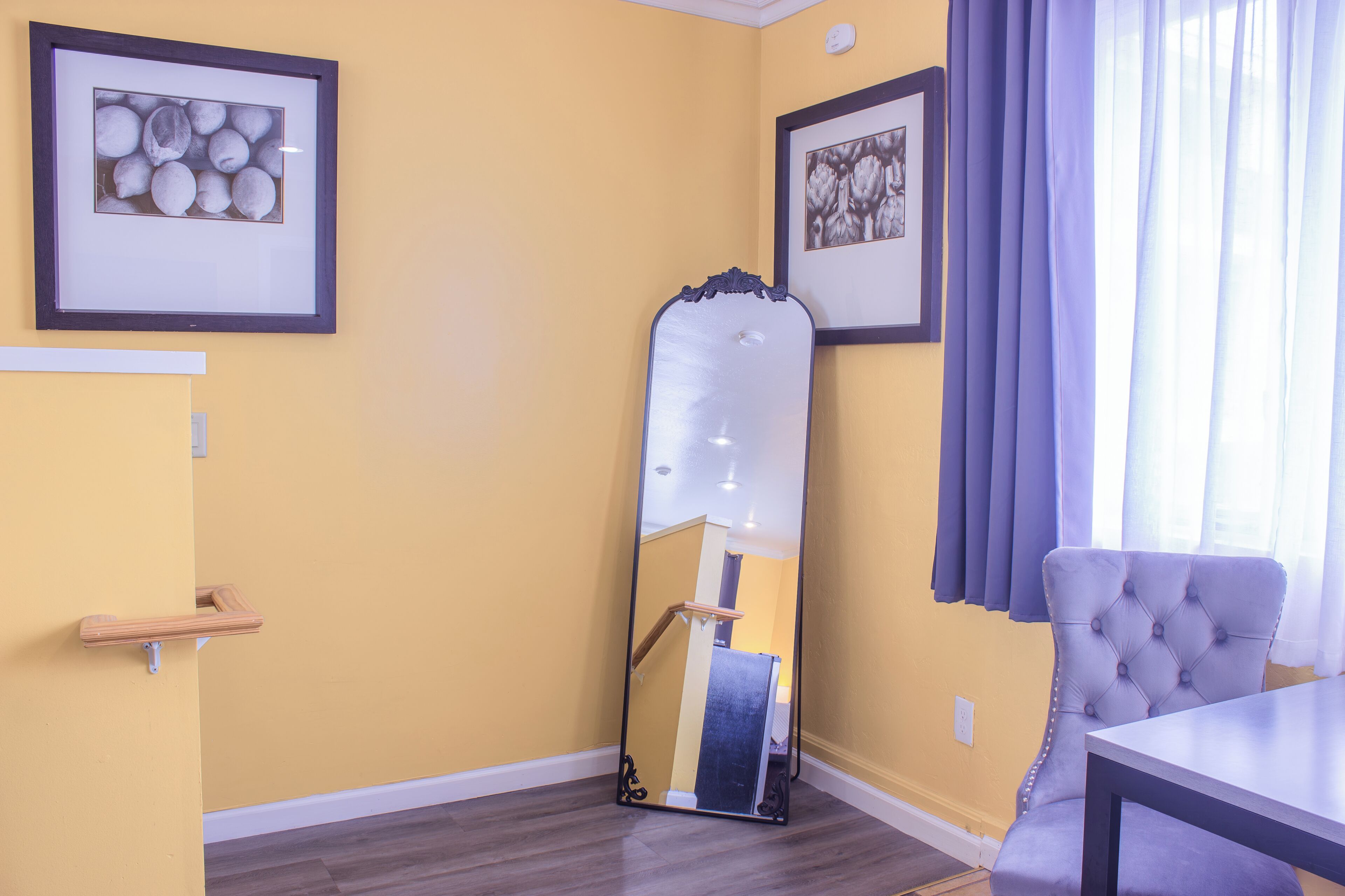 A room with yellow walls, a mirror, a chair, and two framed pictures.