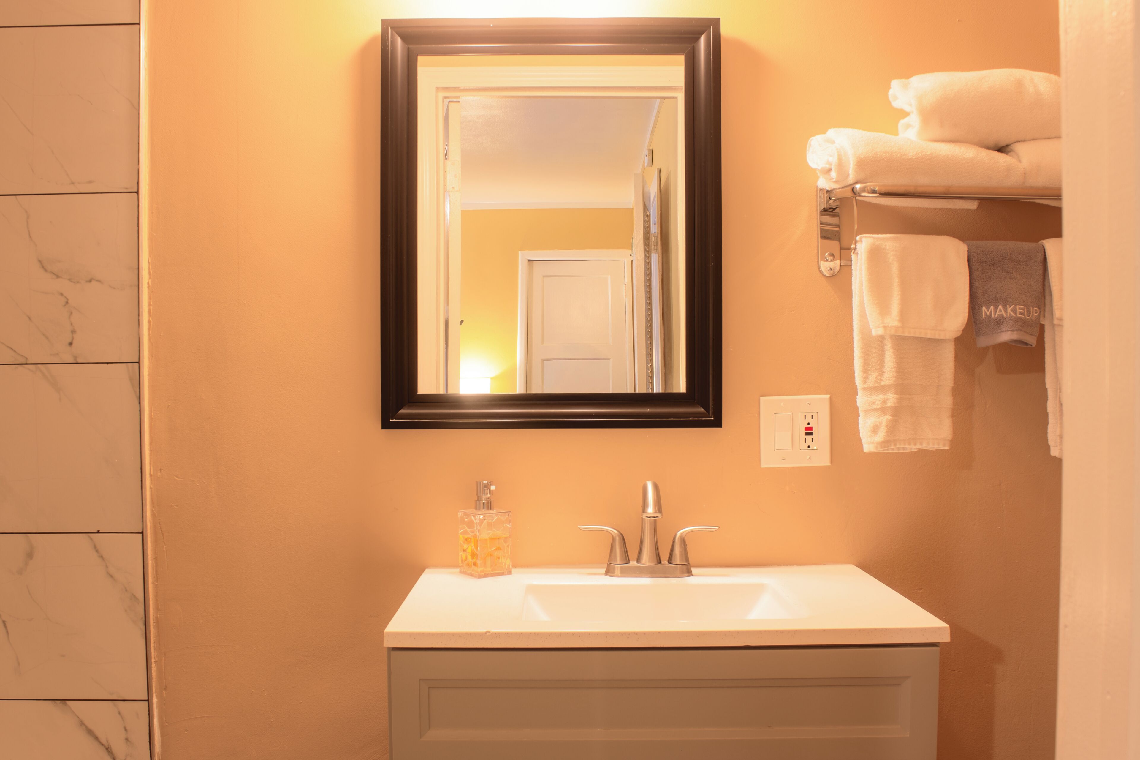 A bathroom with a white sink, a mirror with a black frame, and a towel rack with towels.