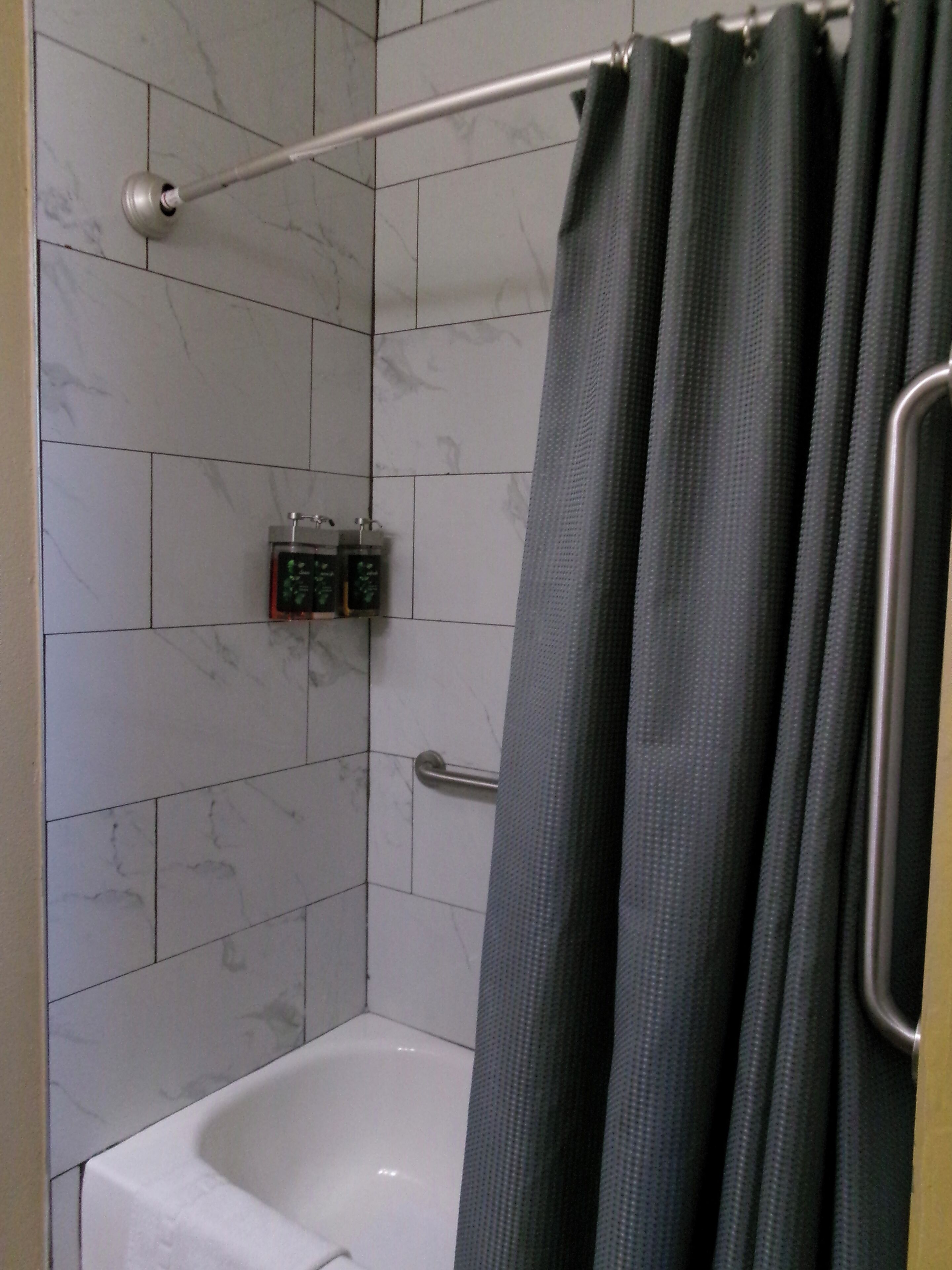 A shower with a handheld showerhead, a glass-enclosed toilet, and a towel rack.