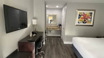A hotel room with a bed, desk, chair, and a television.