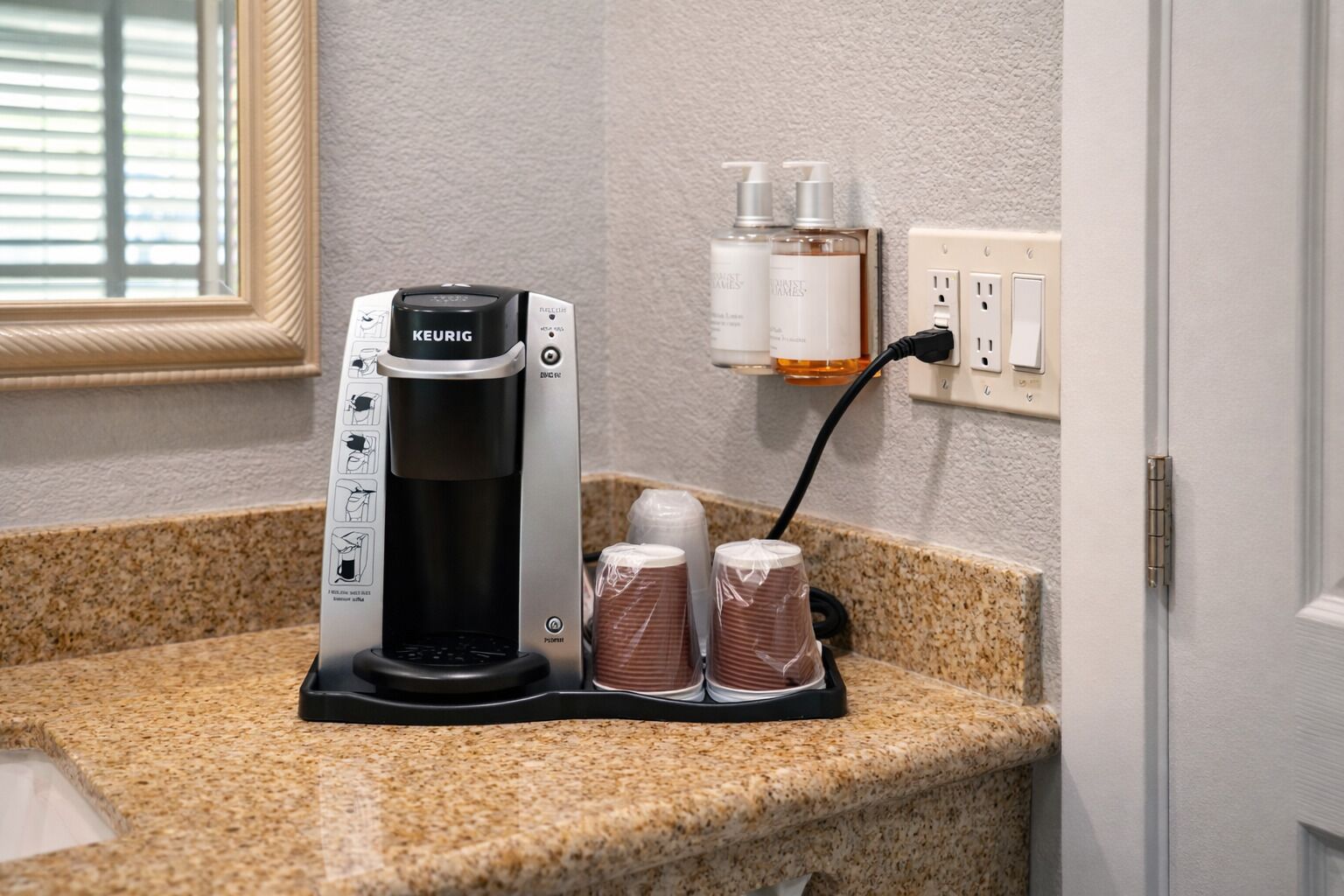 A Keurig coffee maker on a granite countertop with two coffee pods and a bottle of hand soap.