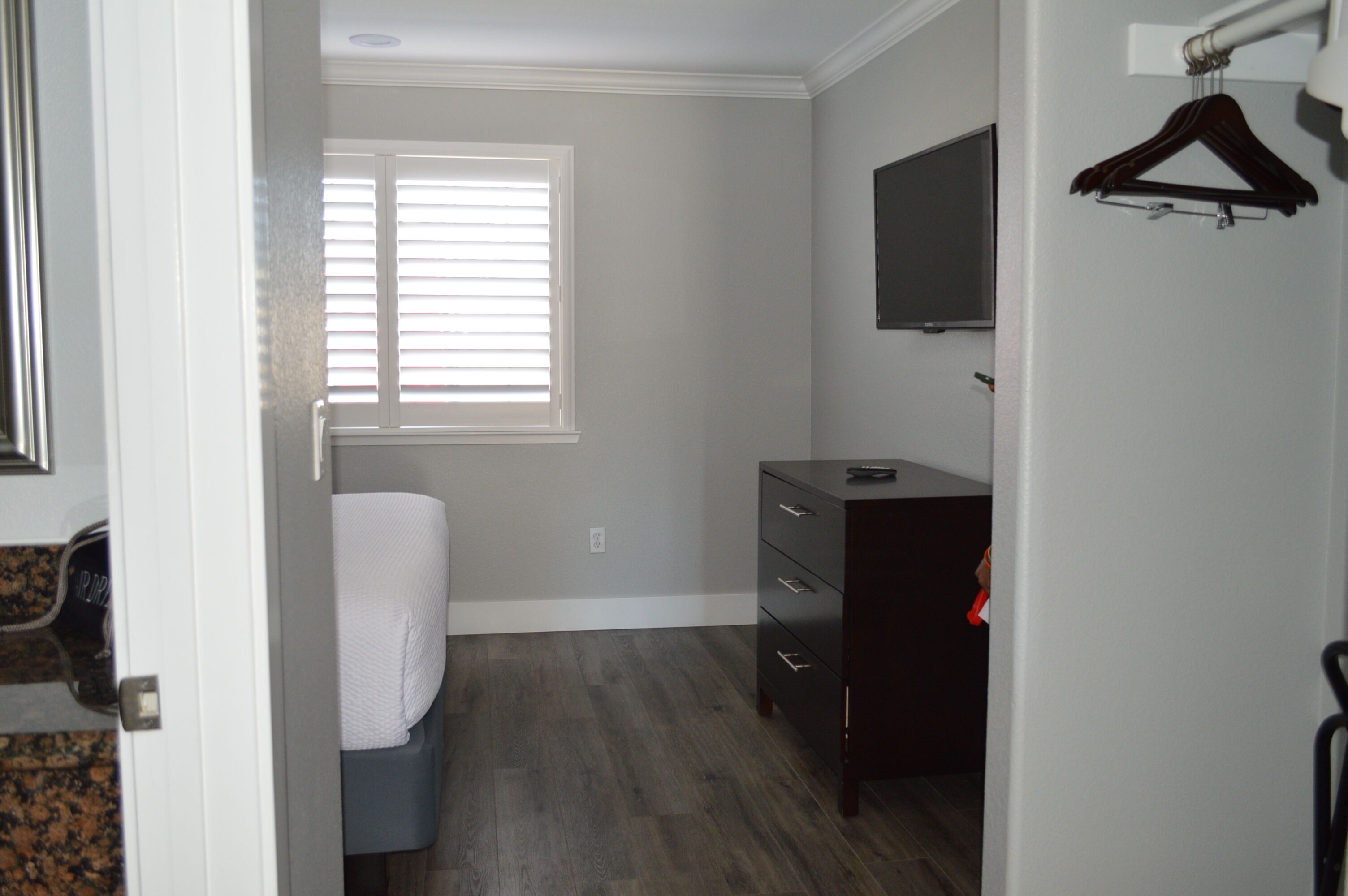 Un dormitorio con cama, cómoda, televisor montado en la pared y ventana con persianas.