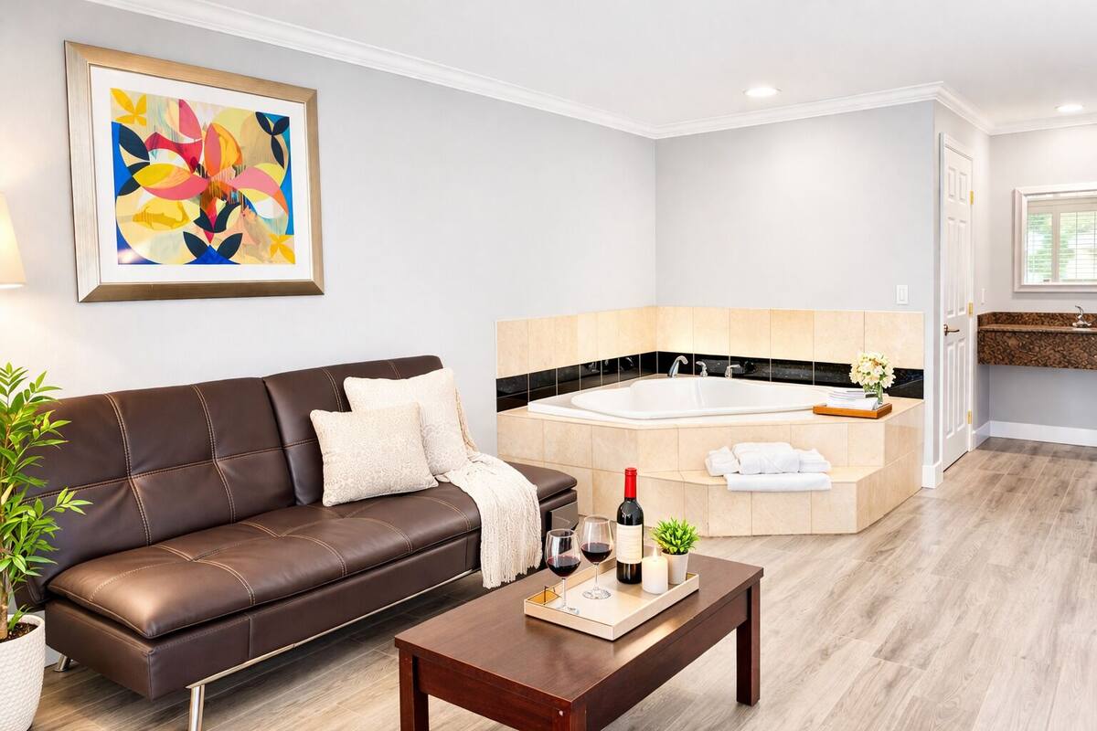 A modern living room with a brown leather sofa, a coffee table with a bottle and glasses, and a large abstract painting on the wall.