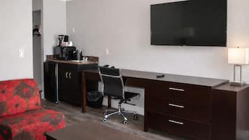 Une chambre d’hôtel compacte comprenant un coin cuisine, un téléviseur à écran plat, un canapé rouge à motifs floraux, un bureau avec des tiroirs et une petite poubelle.