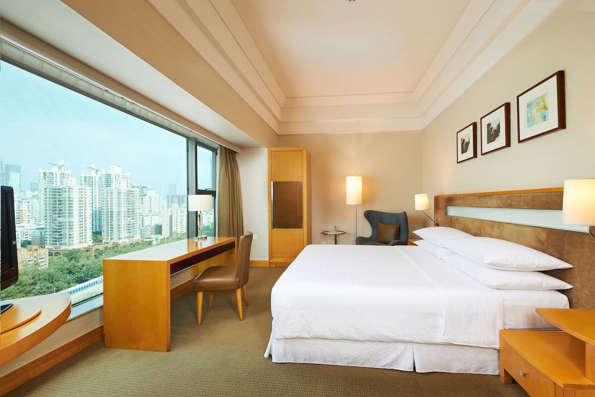 A hotel room with a large bed, a desk, a chair, and a view of the cityscape.