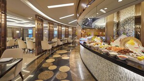 Un moderno vestíbulo de hotel con un mostrador de recepción curvo, zona de comedor con sillas y mesas, y un diseño decorativo en el suelo.