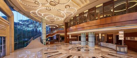 A spacious lobby with a grand staircase, a marble reception desk, and a modern chandelier.