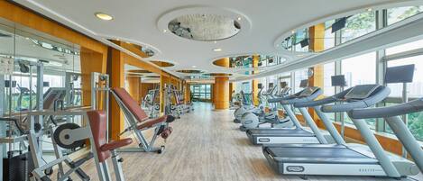 Un gimnasio con cintas de correr, máquinas de pesas y espejos en las paredes.