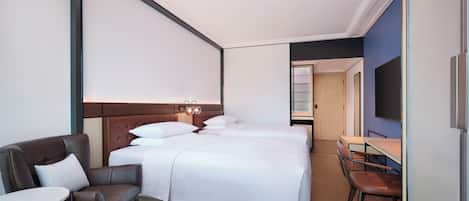 Ett modernt hotellrum med en säng, ett skrivbord, en stol och en tv.