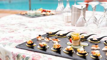 A table with a floral tablecloth and a variety of appetizers and drinks, including a glass with a yellow drink and several glasses of water.