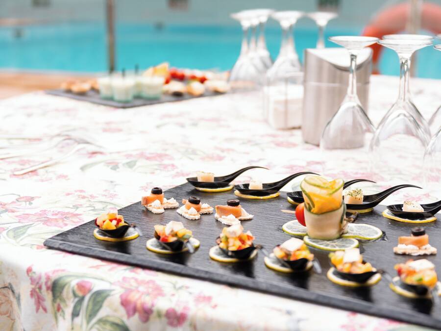 A table with a floral tablecloth and a variety of appetizers and drinks, including a glass with a yellow drink and several glasses of water.