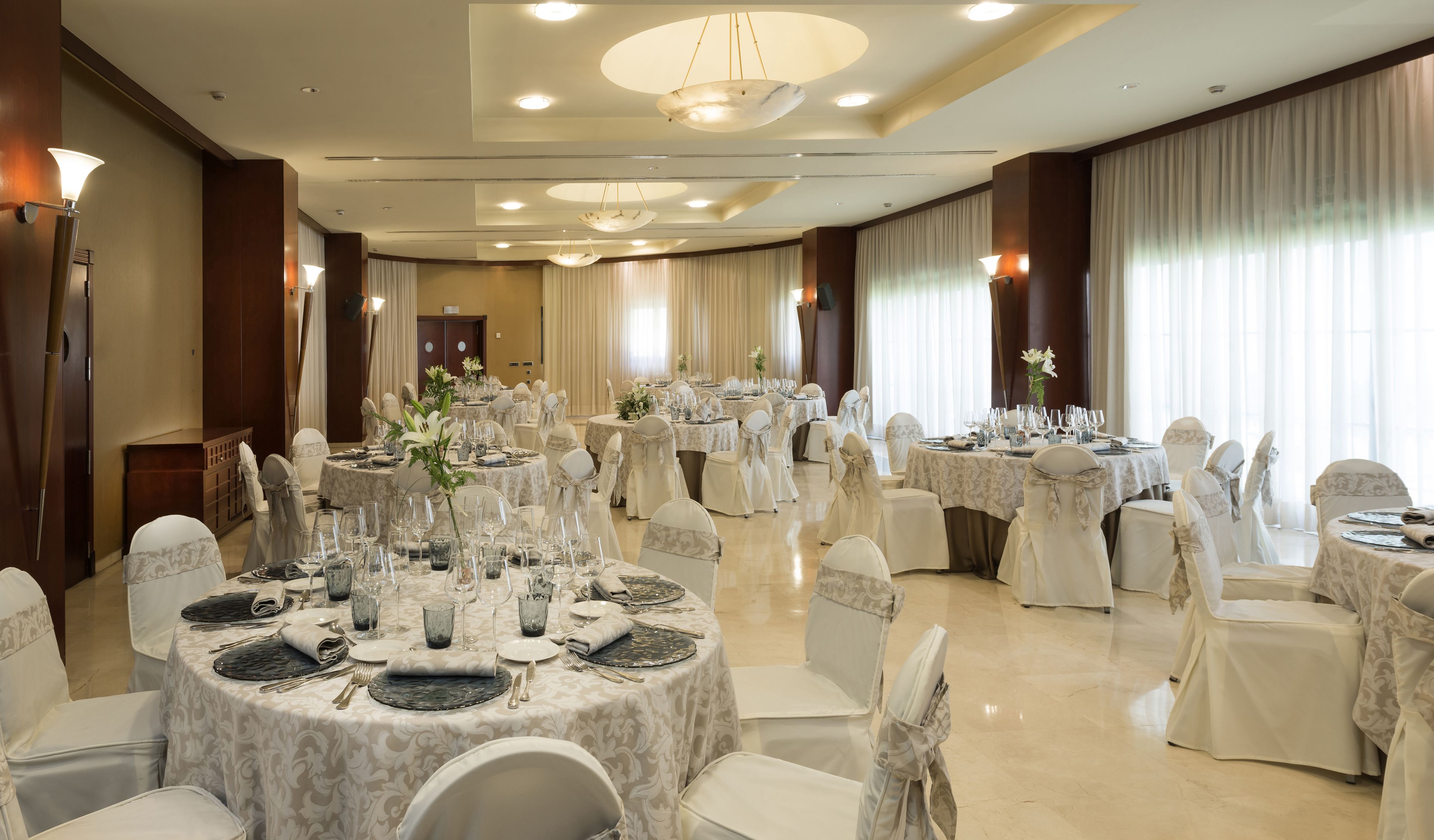 A banquet hall with round tables set for a formal event, featuring white tablecloths, glassware, and floral centerpieces.