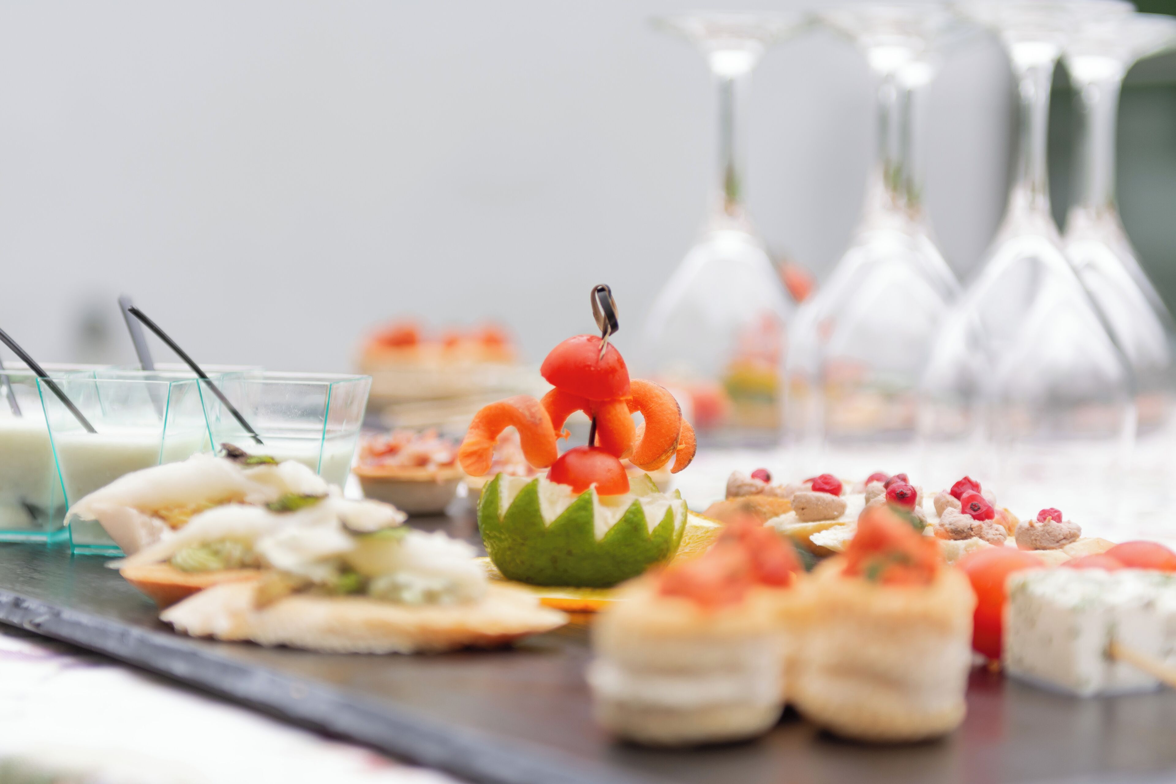 A variety of food items on a buffet table, including a centerpiece with a decorative arrangement of fruits and vegetables.
