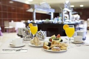 Un bufé de desayuno con diversos pasteles, fruta y zumo de naranja.