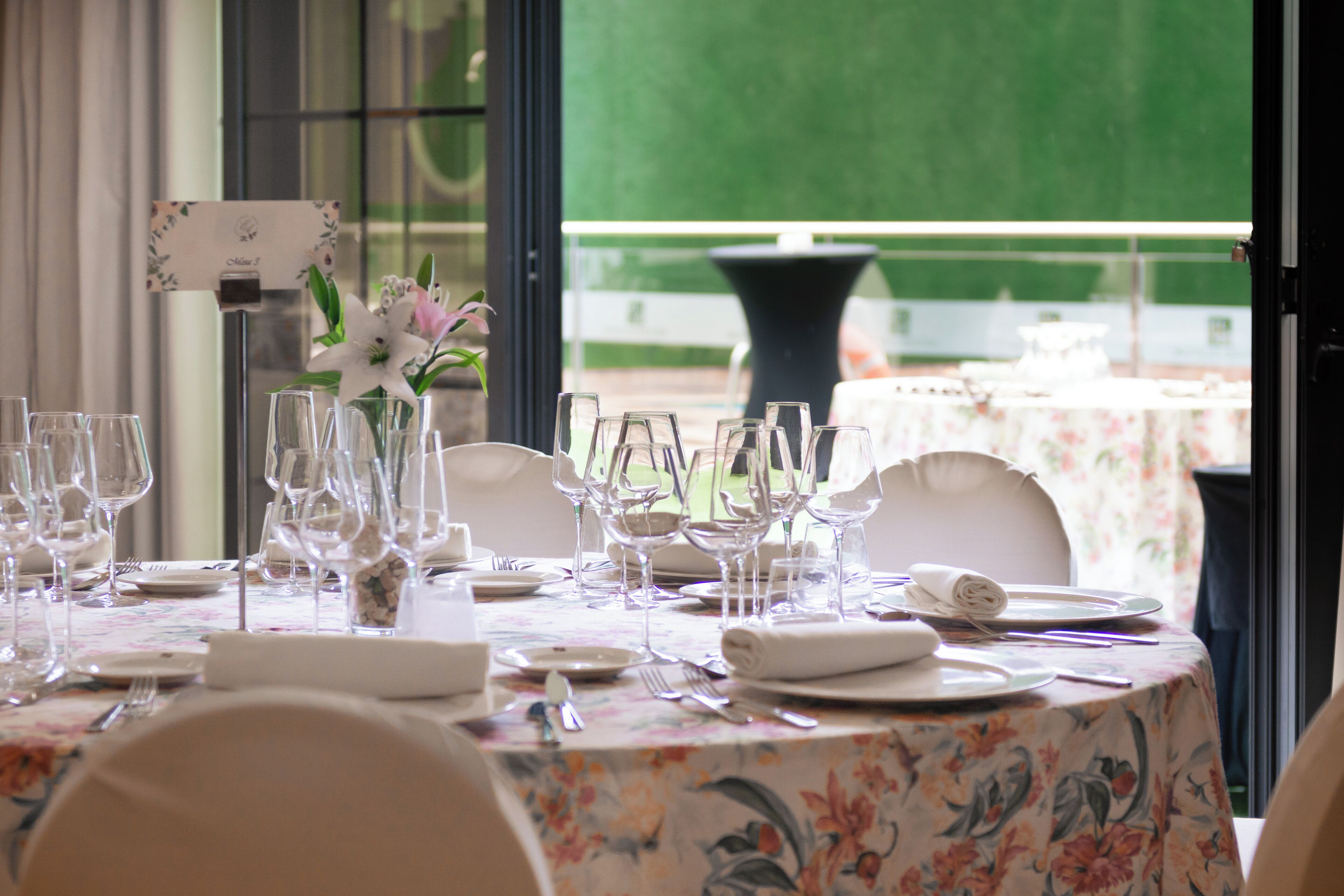 A table set for dining with a floral tablecloth, clear glassware, and white plates.