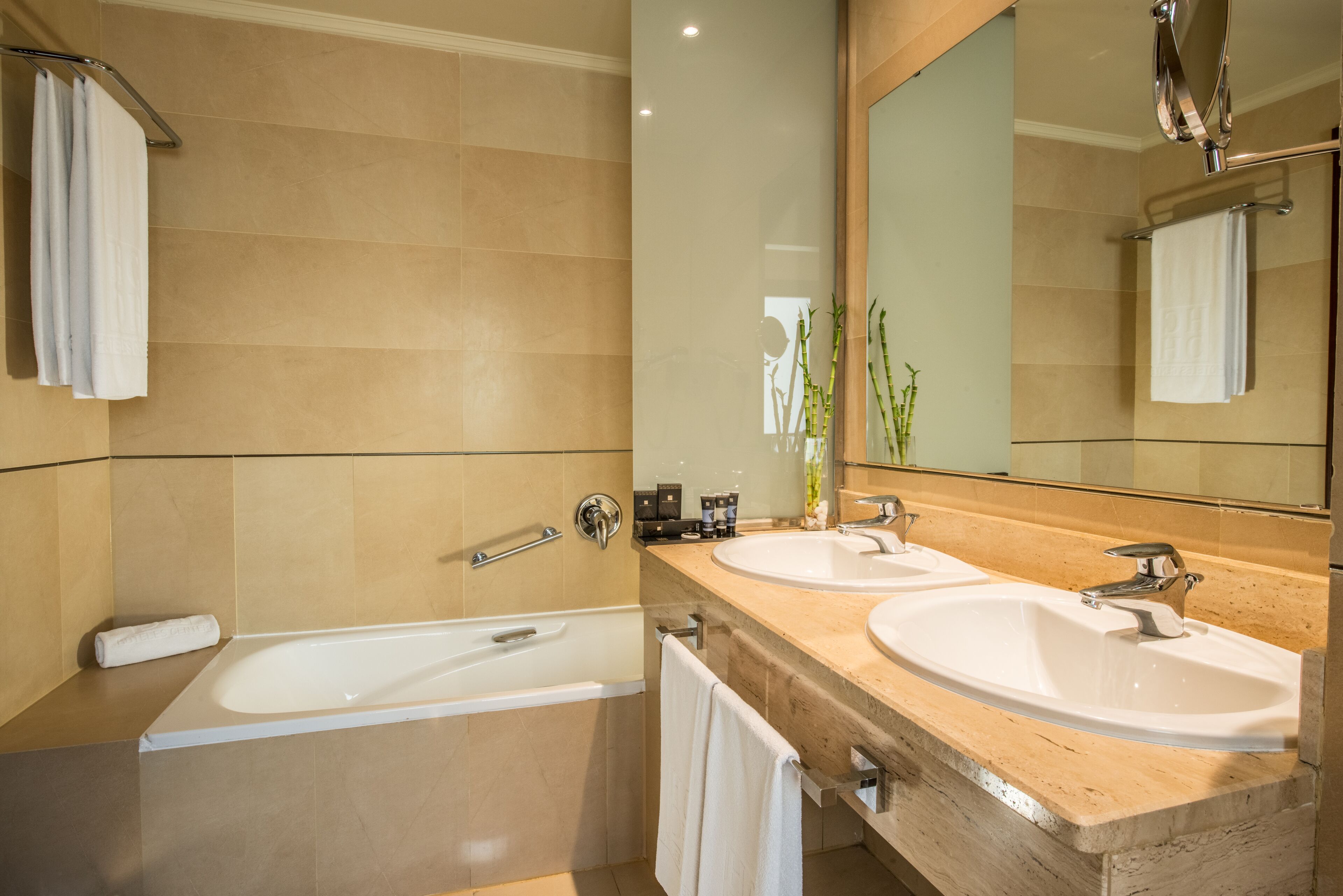 A modern bathroom with a bathtub, two sinks, and a large mirror.