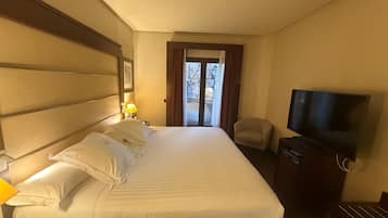 Een hotelkamer met een groot bed, een televisie, een stoel en een raam met gordijnen.