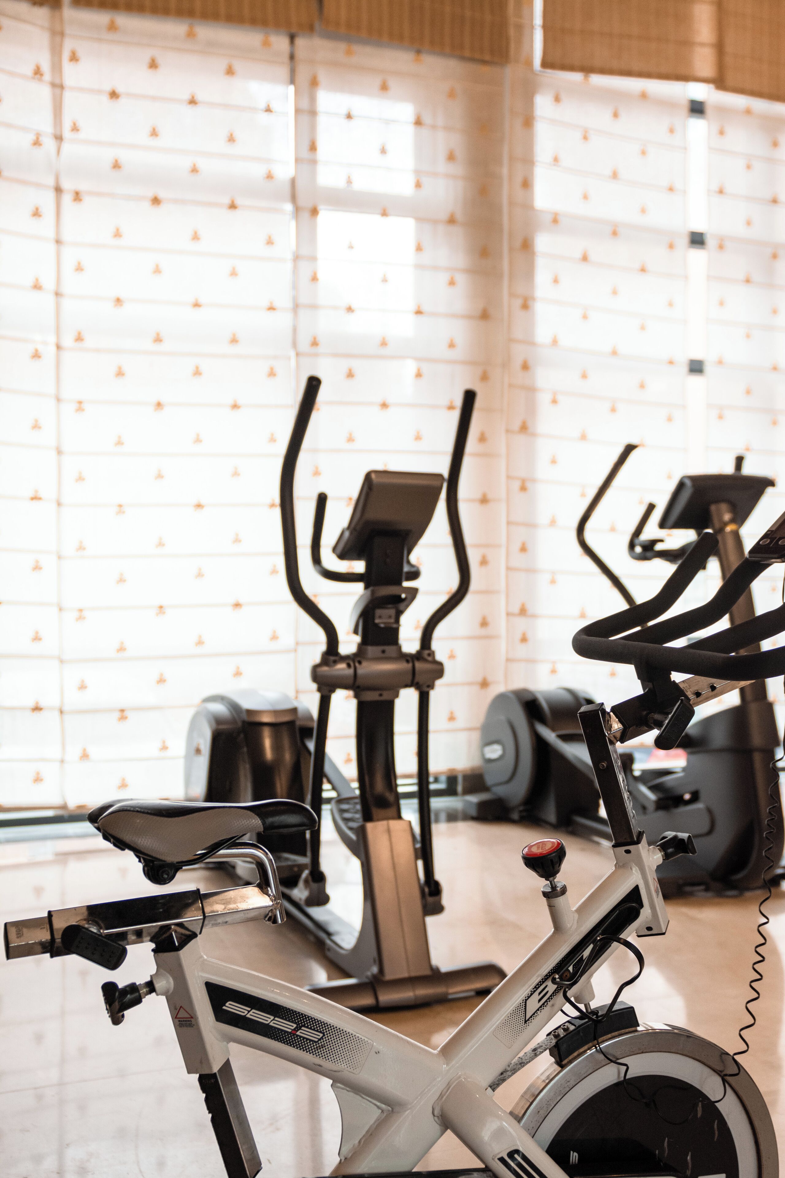 Un vélo d’appartement dans une pièce dont le papier peint est orné de motifs, avec du matériel de musculation en arrière-plan.