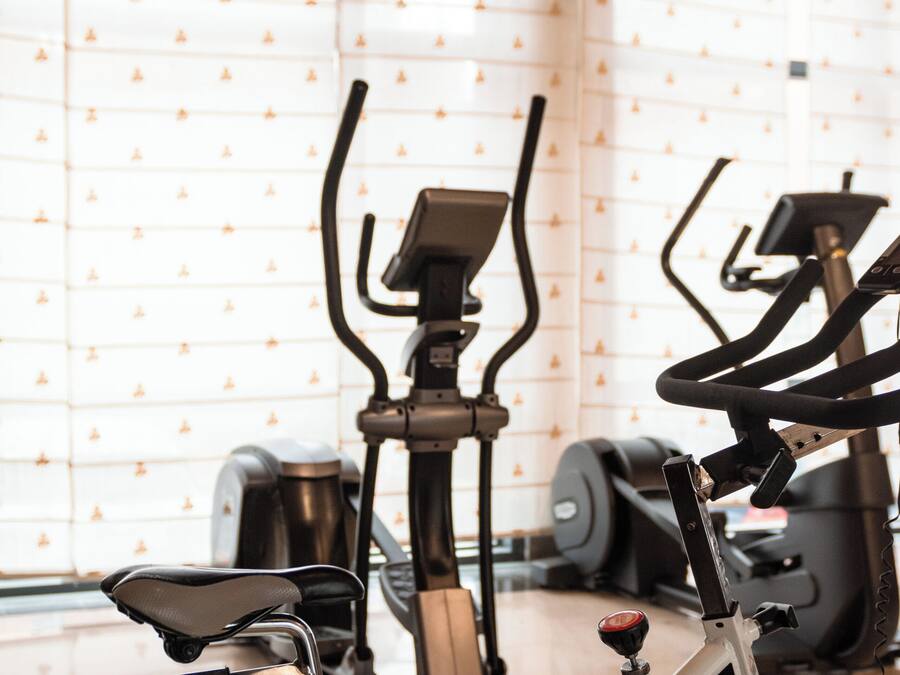 A stationary bike in a room with patterned wallpaper and exercise equipment in the background.