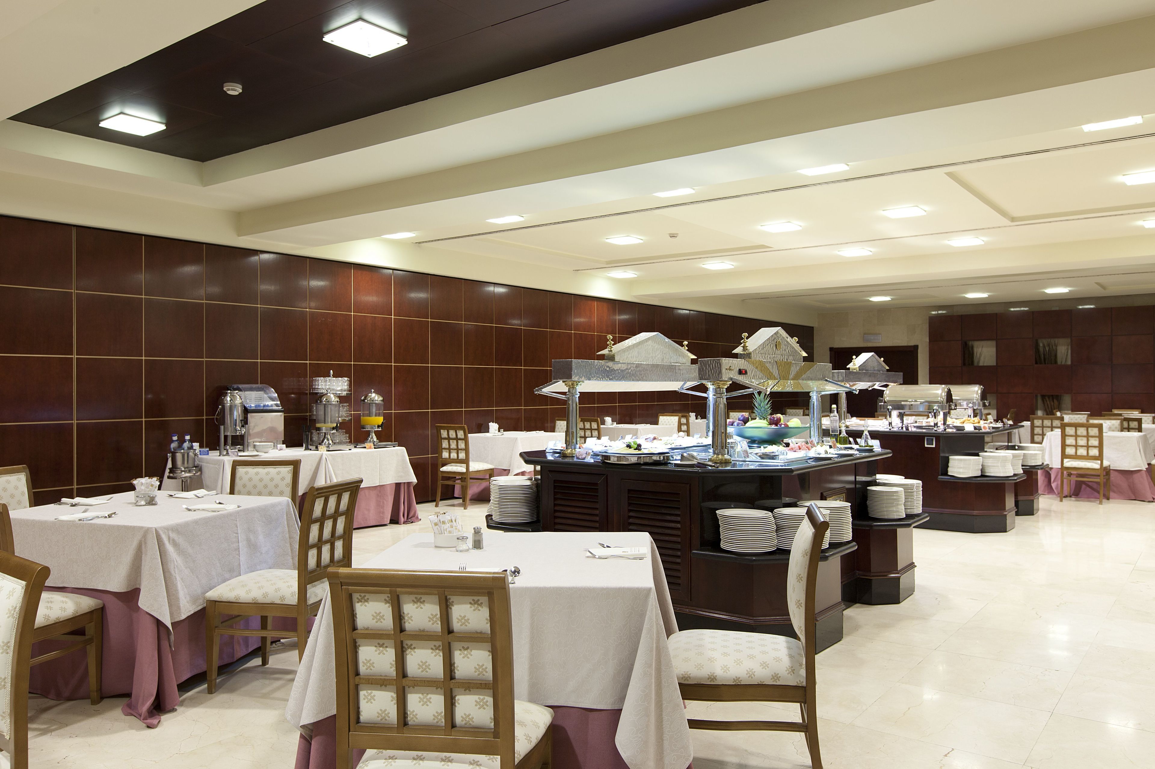 A dining area with multiple tables and chairs, a buffet station, and a kitchen in the background.