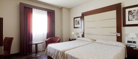 Habitación de hotel con dos camas, un escritorio, una silla, una ventana con cortinas y un cuadro en la pared.