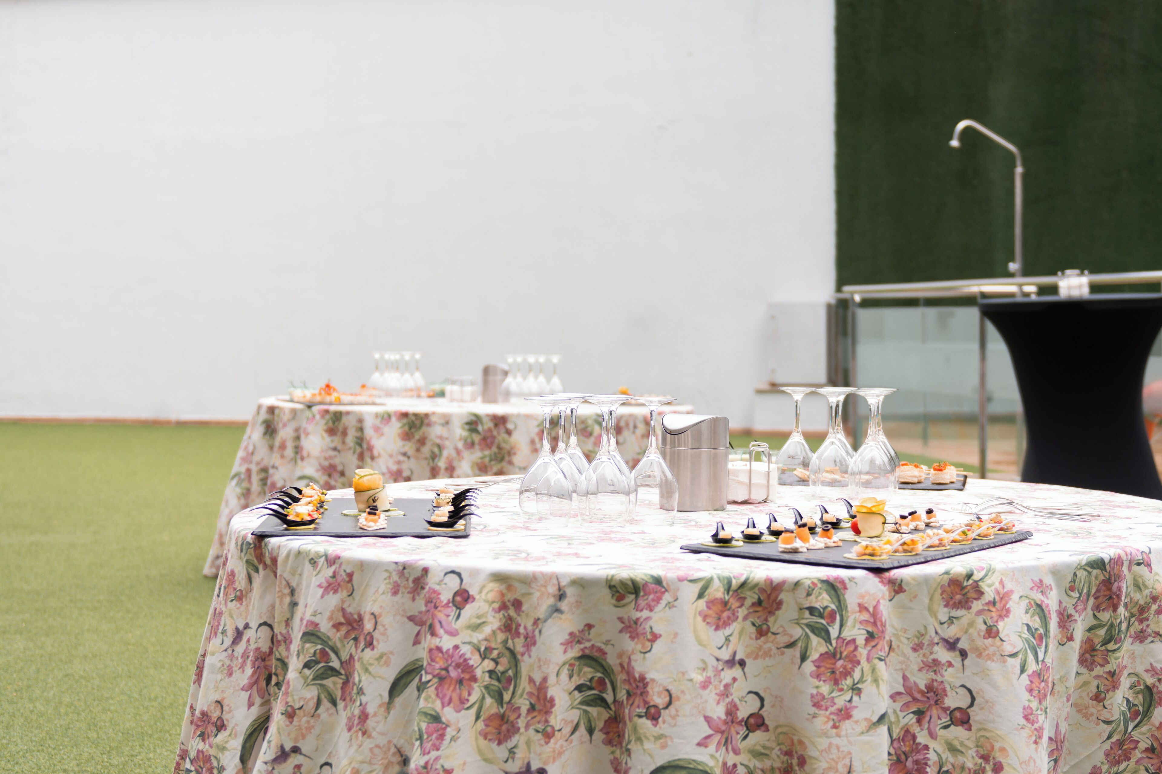 Una mesa dispuesta con mantel floral, copas transparentes y una variedad de aperitivos.
