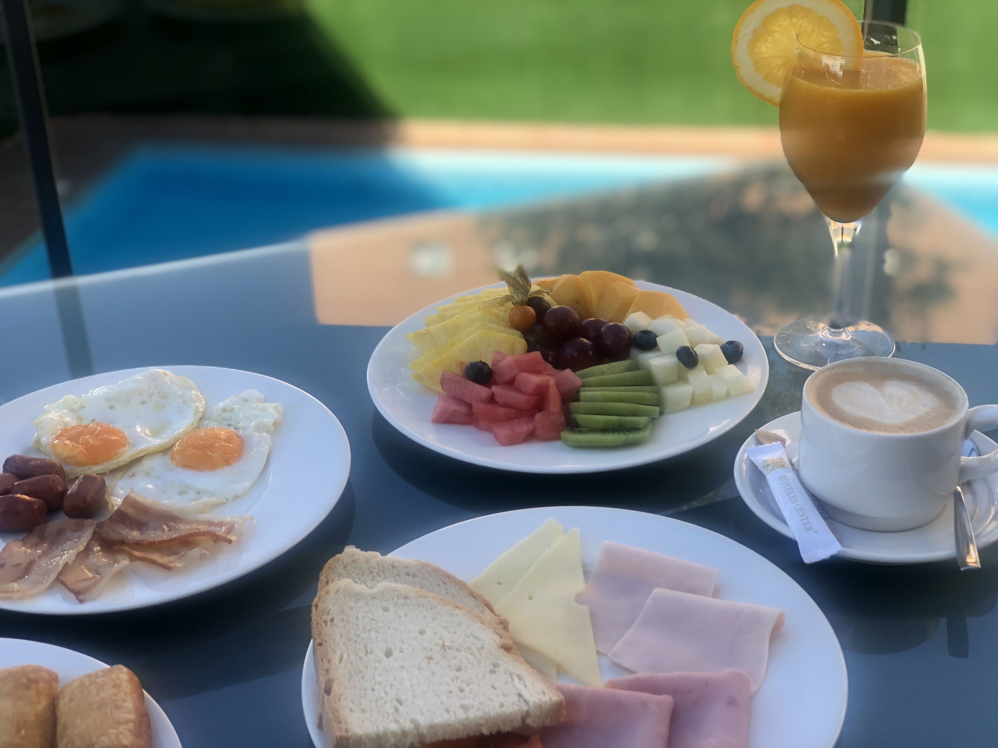 Una mesa de desayuno con platos de huevos, tocino, tostadas, queso, jamón y fruta.
