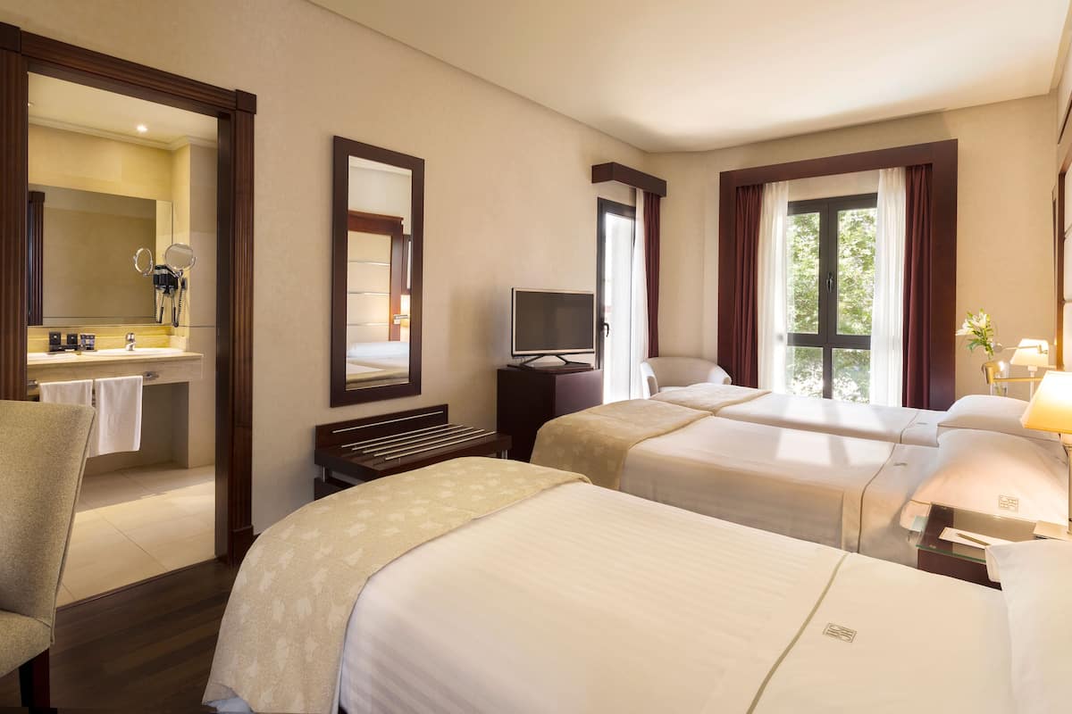 A hotel room with two beds, a TV, a desk, a chair, and a bathroom with a mirror and sink.