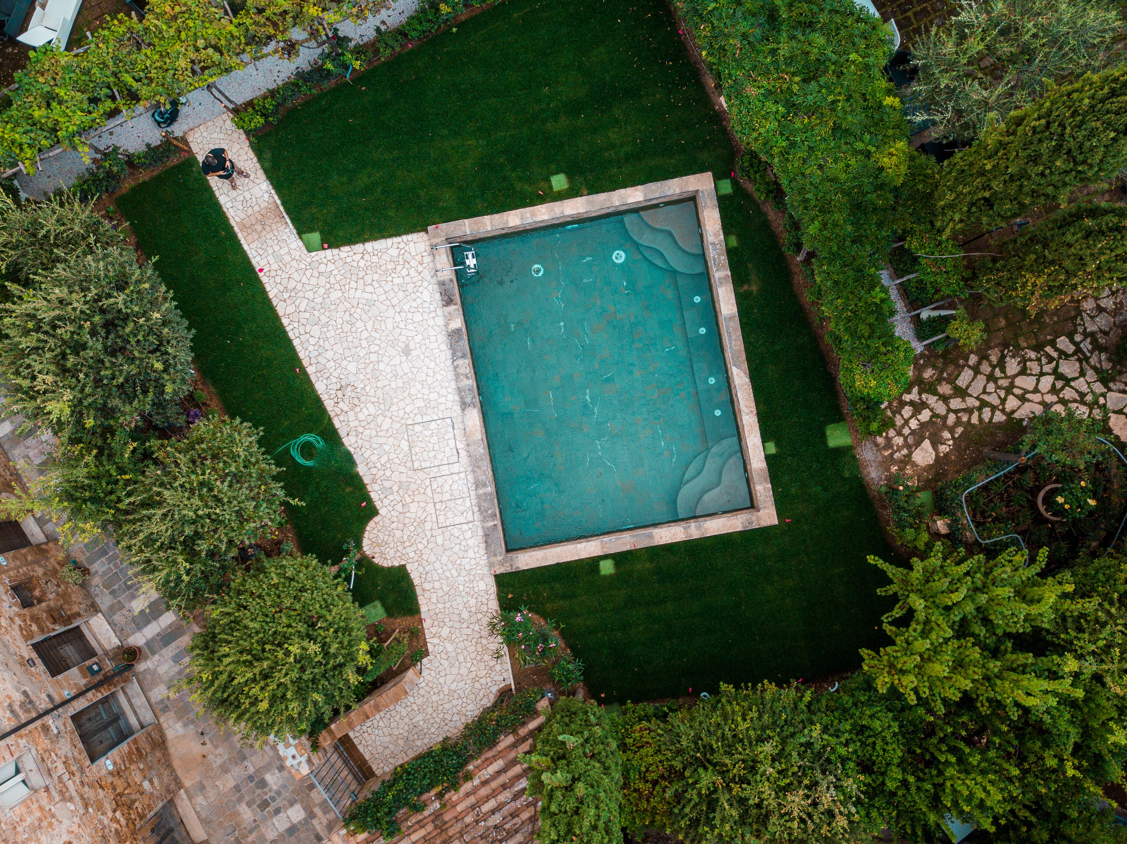 Vista aérea de una piscina rodeada por un patio de piedra y abundante vegetación.