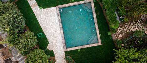 Vista aérea de una piscina rodeada por un patio de piedra y abundante vegetación.