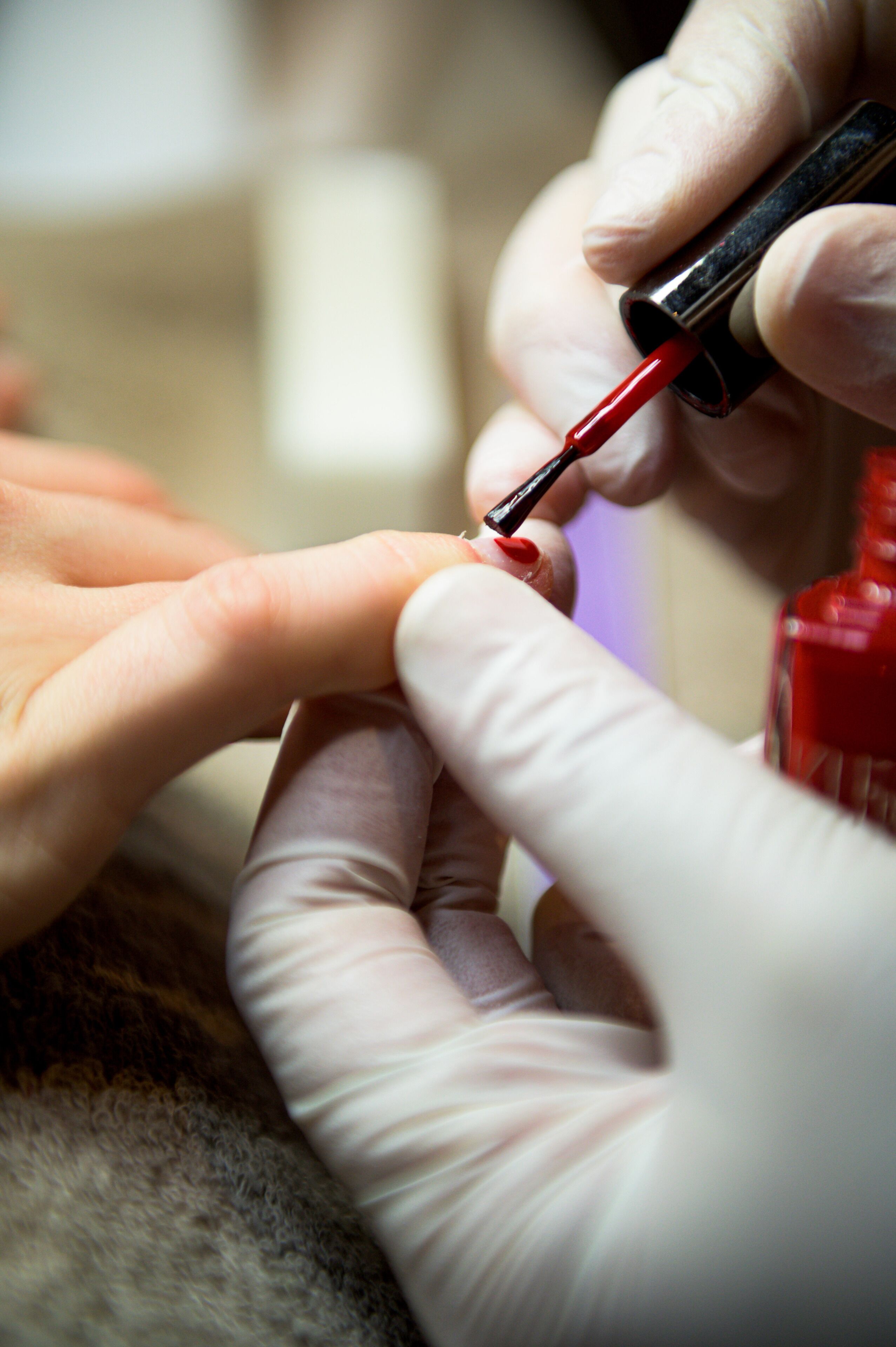 Nahaufnahme einer Person, die roten Nagellack auf die Fingernägel einer anderen Person aufträgt.