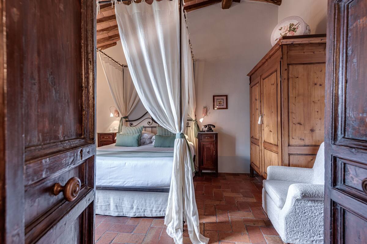 Quarto com cama de dossel, guarda-roupa de madeira e uma cadeira.