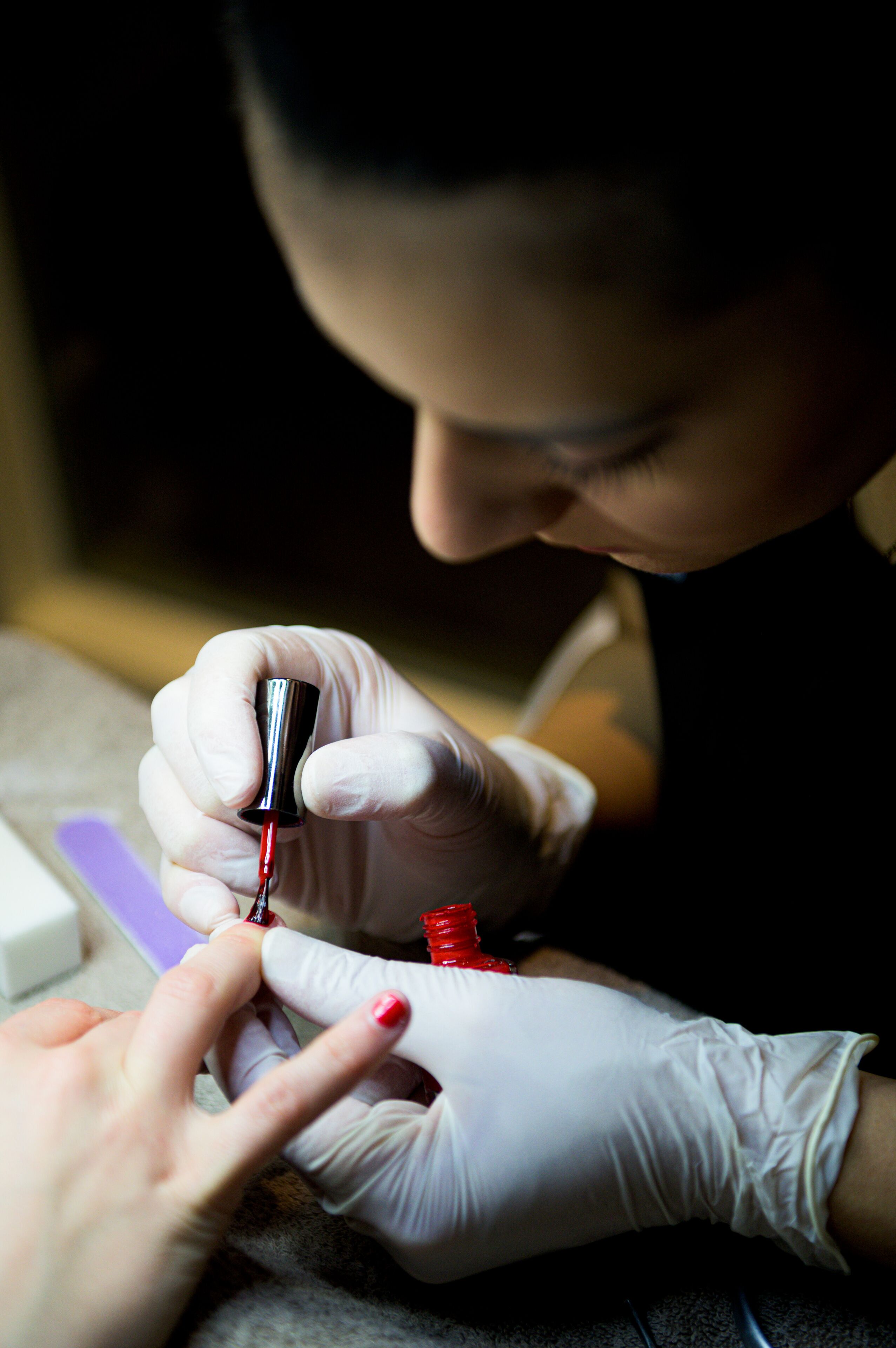 A close-up of a person painting a nail with a red nail polish.