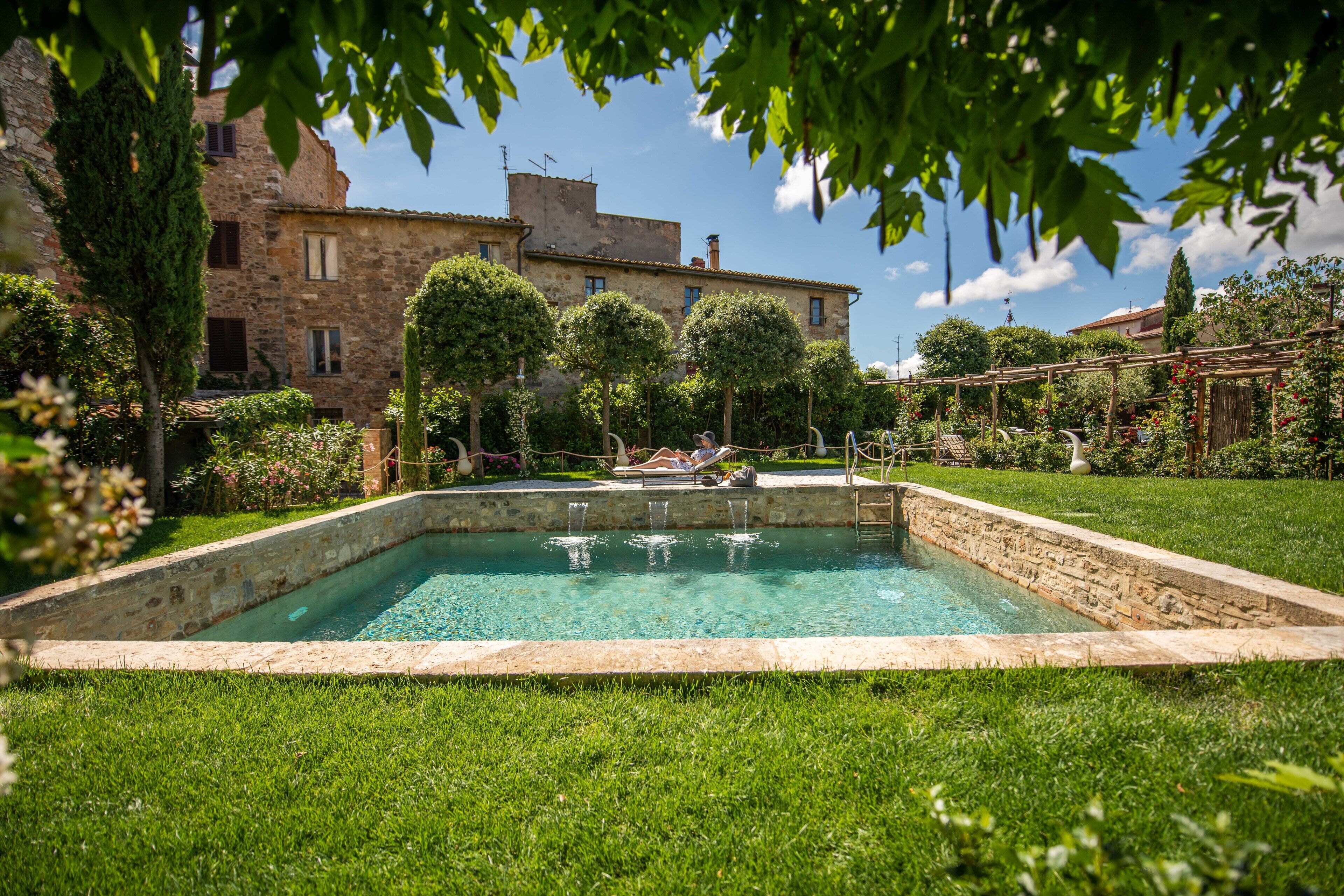 Una piscina rectangular con borde de piedra, rodeada de césped y árboles bien cuidados.