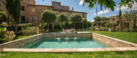Una piscina rectangular con borde de piedra, rodeada de césped y árboles bien cuidados.