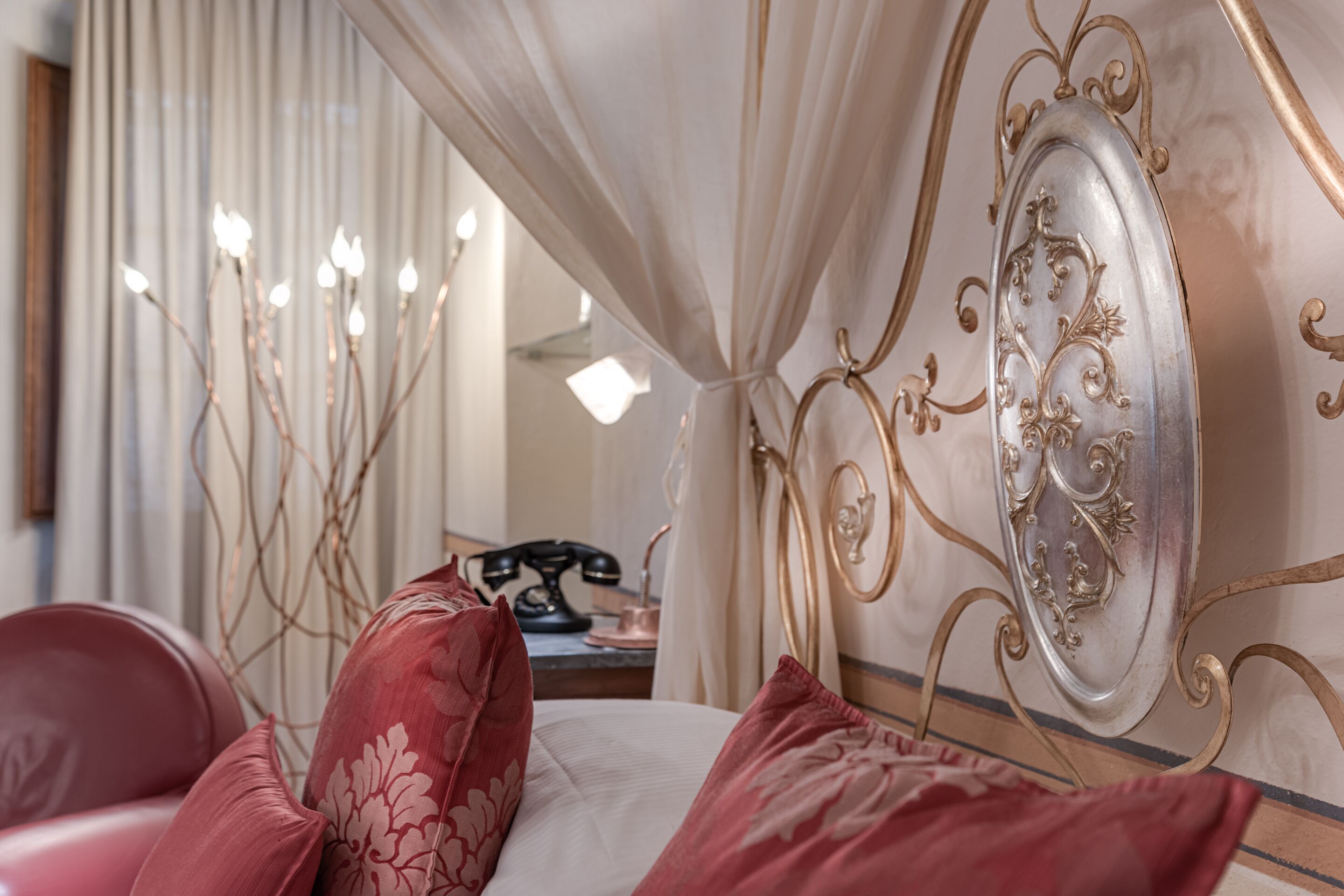 A bedroom with a bed, red pillows, a bedside table with a lamp, and a mirror.