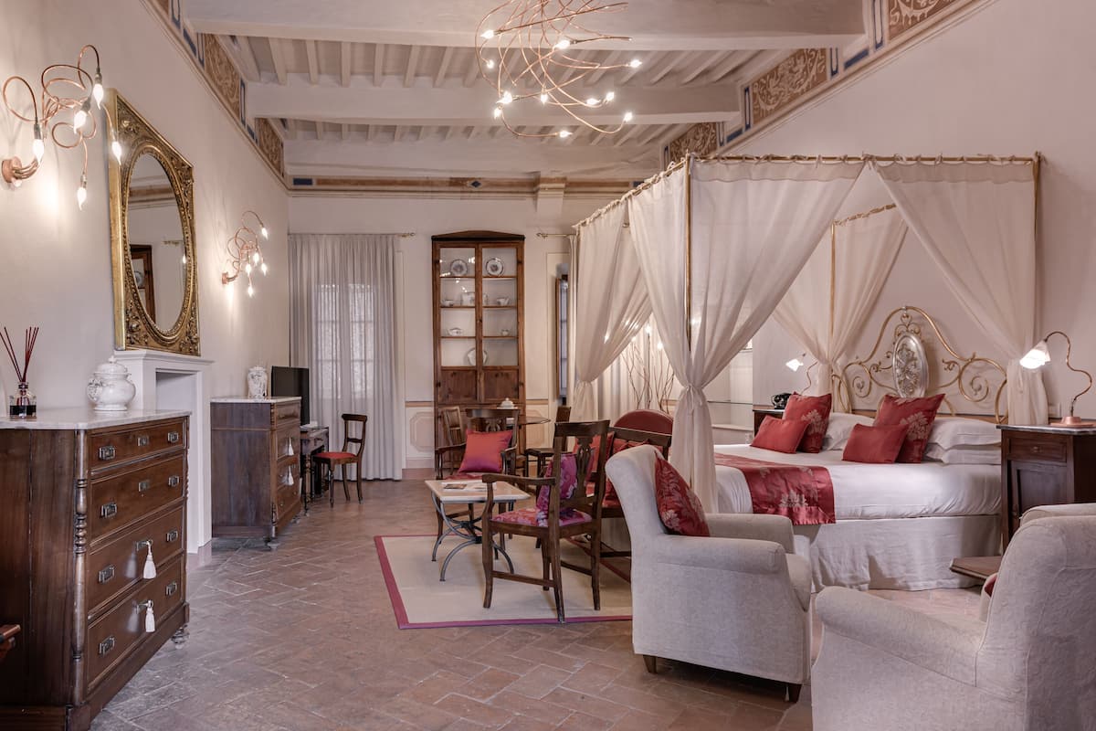 Quarto de hotel com uma cama grande, um espaço de estar com cadeiras, um armário de madeira e um espelho amplo.