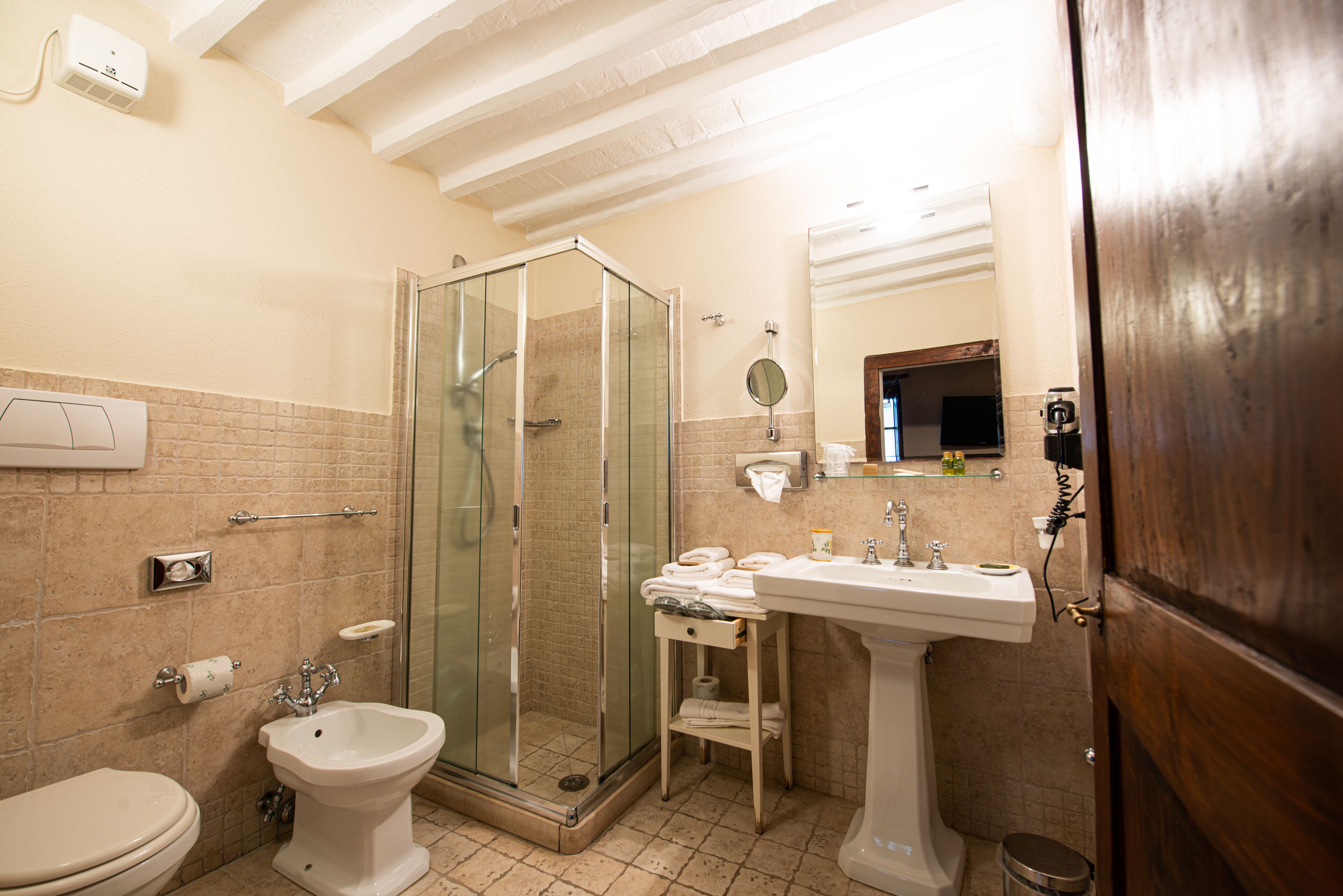 Un baño con ducha de vidrio, lavamanos pedestal, inodoro y un perchero para toallas.