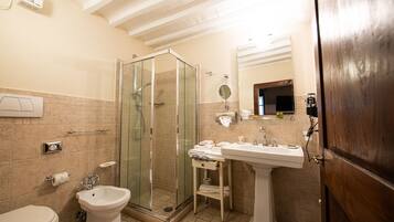 Un baño con ducha de vidrio, lavamanos pedestal, inodoro y un perchero para toallas.