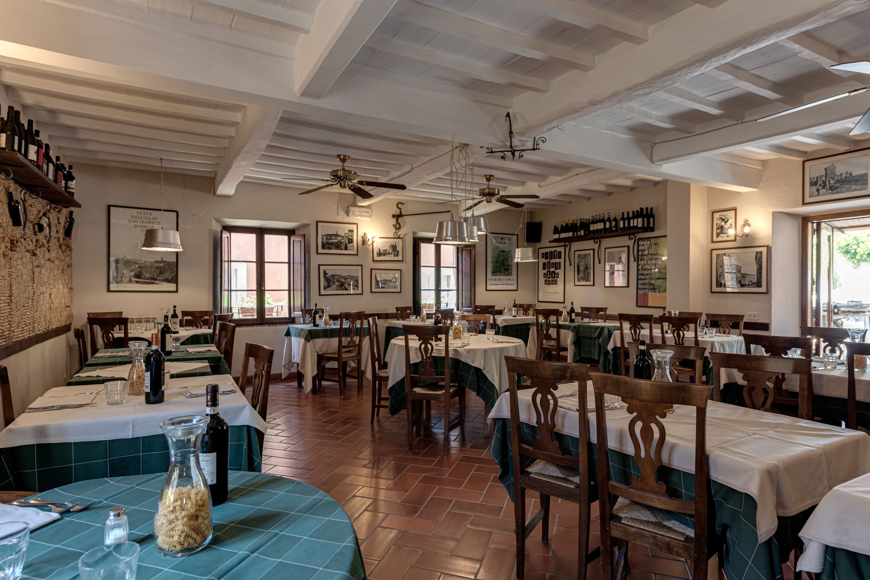 A restaurant with multiple tables and chairs, ceiling fans, and framed pictures on the walls.