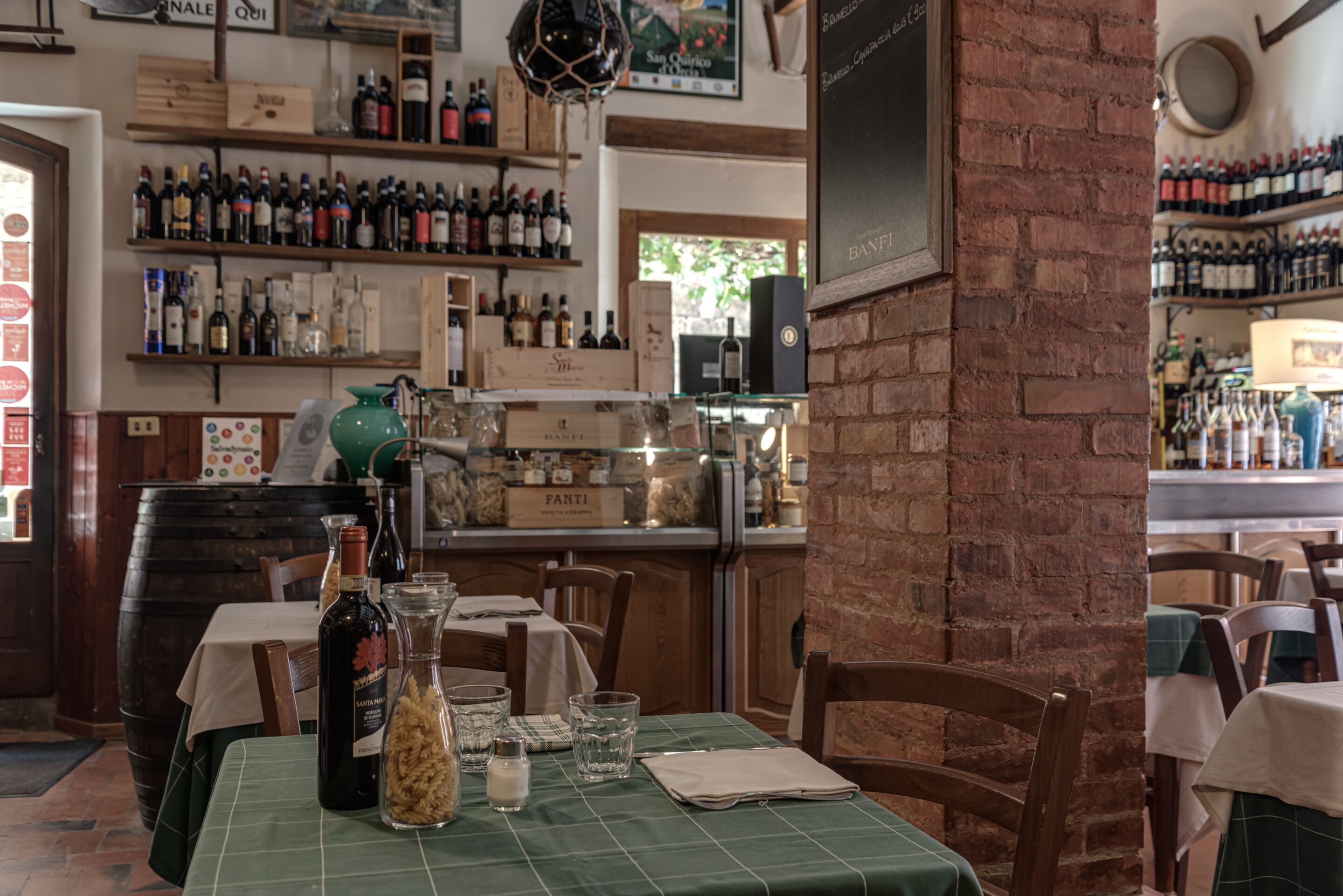 Een restaurant interieur met bakstenen muren, houten tafels en planken vol wijnflessen.