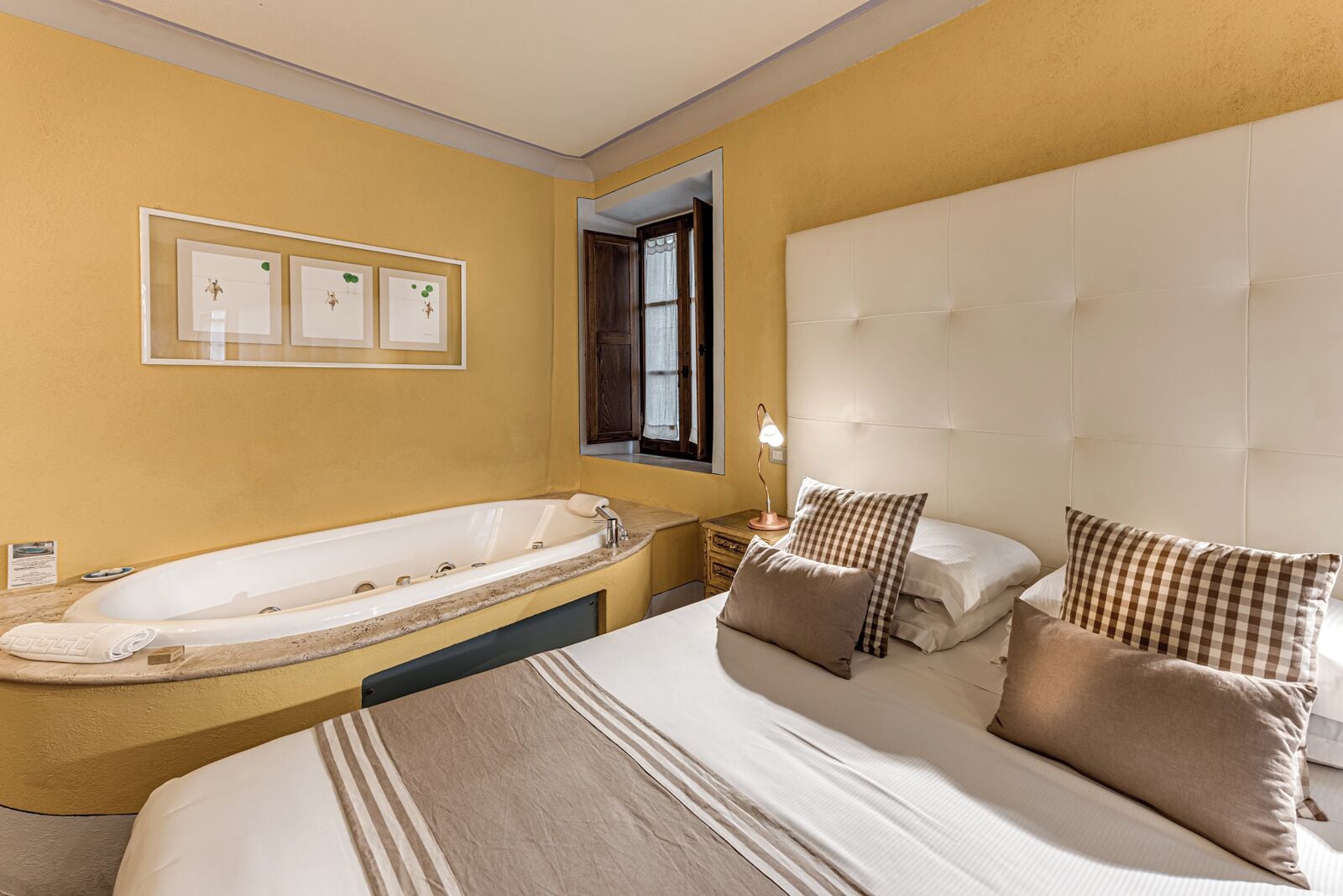 A hotel room with a large bed, a separate bathtub, a bedside table with a lamp, and a window with curtains.