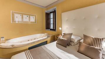 A hotel room with a large bed, a separate bathtub, a bedside table with a lamp, and a window with curtains.