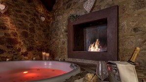 A stone-walled room with a large bathtub, a fireplace, and a tray with a champagne bottle and glasses. -  Hotel Palazzo del Capitano Wellness & Relais - Luxury Borgo Capitano Collection (San Quirico d'Orcia)