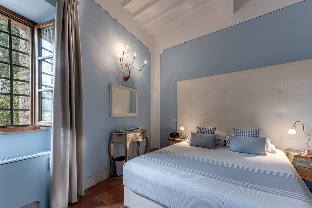 Quarto com uma cama grande, mesa de cabeceira, escrivaninha e janela com cortinas.