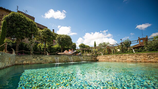 A clear pool with a stone wall and a wooden bridge. -  Hotel Palazzo del Capitano Wellness & Relais - Luxury Borgo Capitano Collection (San Quirico d'Orcia)