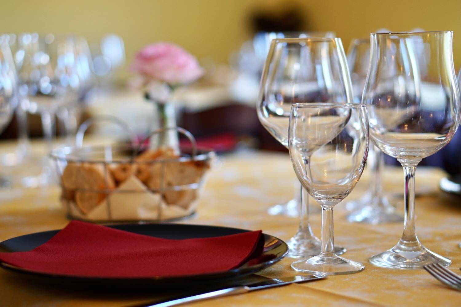 A table set with wine glasses, a red napkin, and a basket of bread.