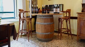 A bar area with a wooden barrel, two wicker bar stools, and several bottles of wine on a table. - Albergo Centrale (Fino del Monte)