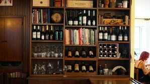 A wine cellar with shelves of wine bottles and glasses, wooden bookshelves, and a vintage Bellavista wine box. - Albergo Centrale (Fino del Monte)